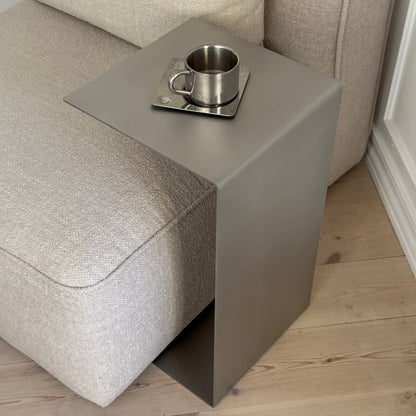 Elegance Side Table positioned over an armchair, showing its slender form and balanced geometry.