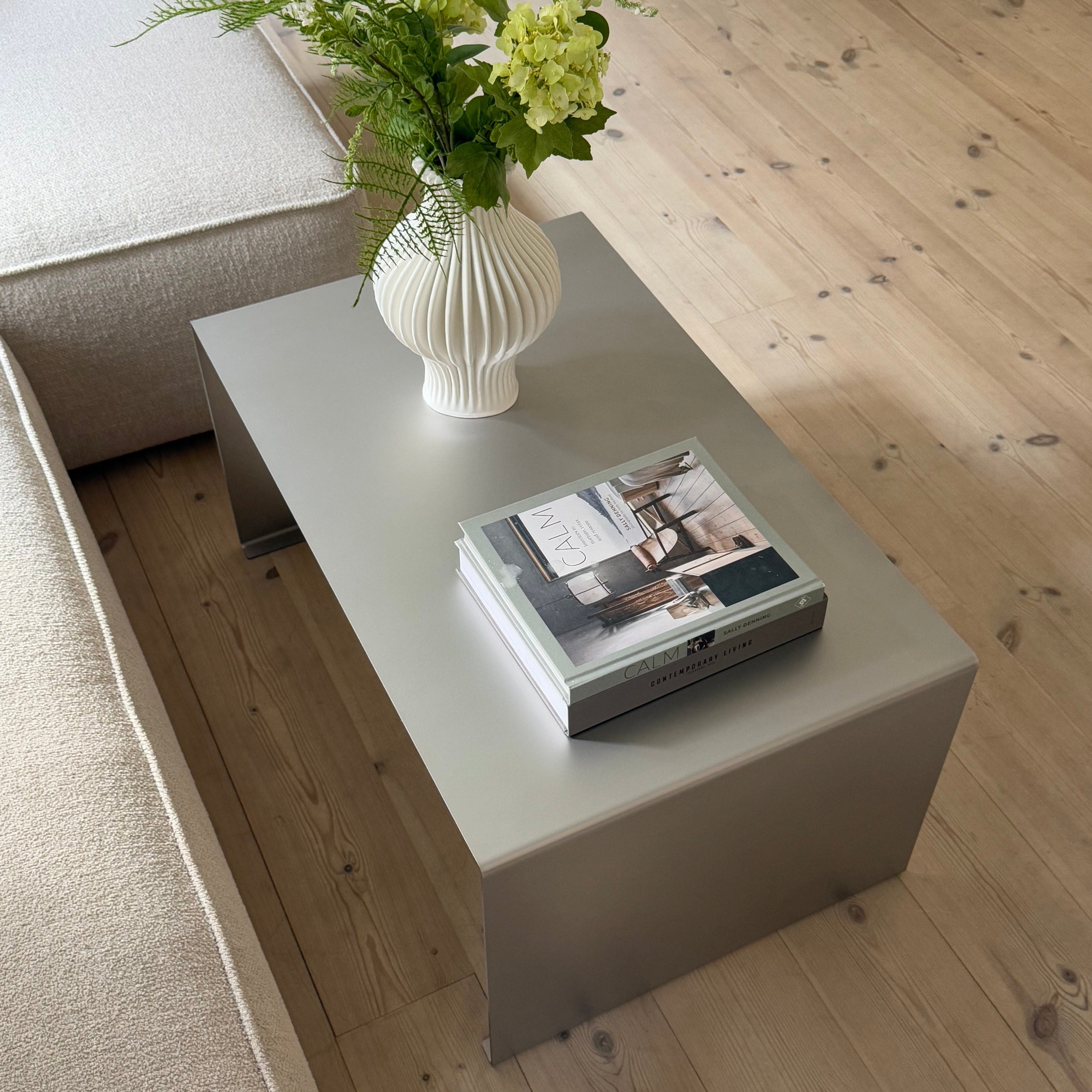 Metal coffee table in satin matte stainless steel styled with books and a white ceramic vase.