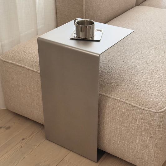 Elegance steel side table in satin matte stainless steel beside a sofa.